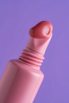 Pink lip gloss tube with creamy texture on purple background
