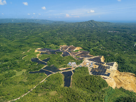 Aerial view of Sikatuna Solar Power Plant featuring rows of solar panels integrated into a lush, hilly landscape with dense forest and clear blue sky in Sikatuna, Central Visayas, Philippines.