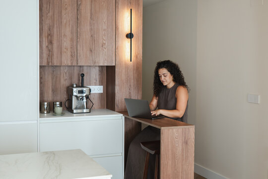Woman using laptop at kitchen counter in modern apartment