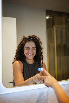 Smiling woman apply skincare in modern apartment bathroom