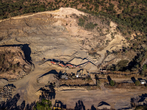 Aerial view of an active quarry with heavy machinery, piles of gravel, and surrounding bushland in Calcium, Queensland, Australia.