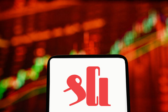 A smartphone displaying the Shree Cement company logo is shown against a blurred red and green stock market candlestick chart background in an editorial finance concept image.
