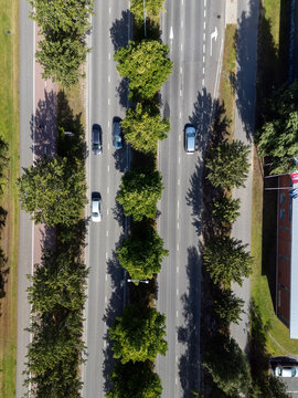 Aerial view of a road with cars driving between rows of green trees and a bicycle path on the side in Oulu, North Ostrobothnia, Finland.