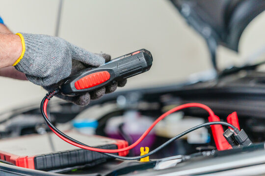 Mechanic using tester to check electric vehicle EV battery voltage under open hood in garage
