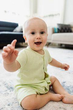 Smiling baby point finger while sit on living room rug