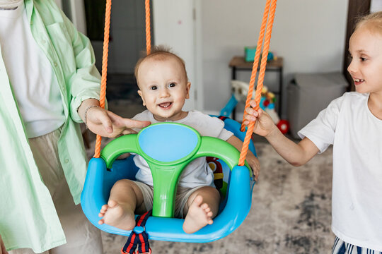 Mother and daughter help baby on indoor swing at home