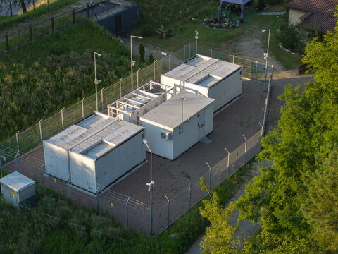 Aerial view of a Battery Energy Storage System with white containers, security fencing, and lighting poles in a rural area in Poland.