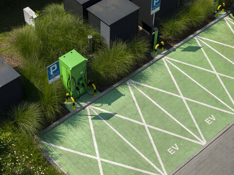 Aerial view of an electric vehicle charging station with green parking spaces and white markings surrounded by ornamental grasses in Krakow, Lesser Poland Voivode, Poland.