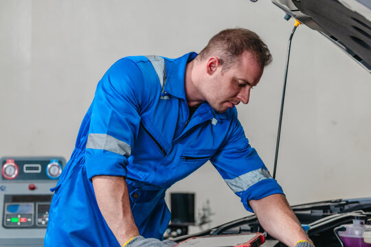 Mechanic using tester to check electric vehicle EV battery voltage under open hood in garage