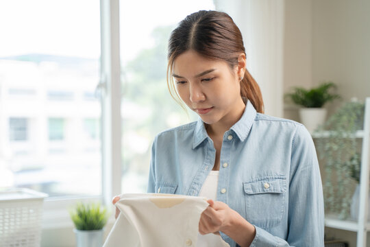 Housewife, asian young woman hand in holding shirt, showing making stain, spot dirty or smudge on clothes, dirt stains for cleaning before washing, making household working at home. Laundry and maid.
