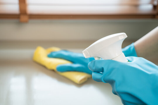 Housekeeper doing chores concept, Close-Up view of housemaid cleaning furniture surface with sanitizer spray and wiping with wet cloth in living room.