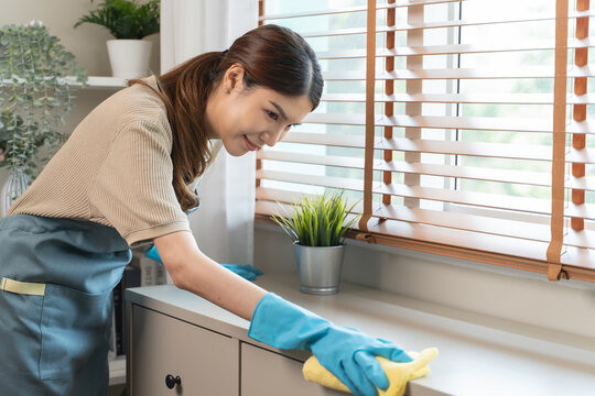 Housekeeper doing chores concept, Close-Up view of housemaid cleaning furniture surface with sanitizer spray and wiping with wet cloth in living room.