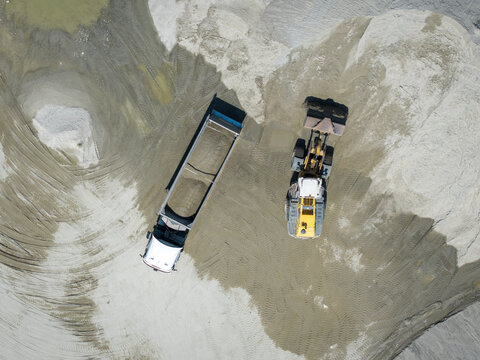 Aerial view of a gravel pit with a dump truck and a front-end loader parked on piles of sand and gravel in Poland.