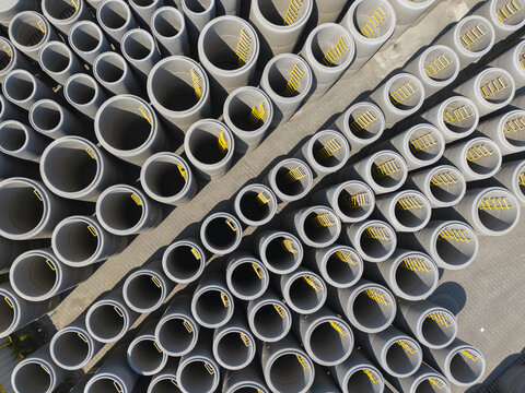Aerial view of concrete pipes with yellow ladders arranged in rows at a construction supply yard in Poland.