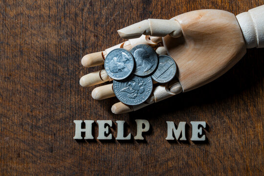 Top view of wooden mannequin hand holding American quarter and half dollar coins next to text help me on dark rustic wooden background, closeup. Financial crisis and charity concept