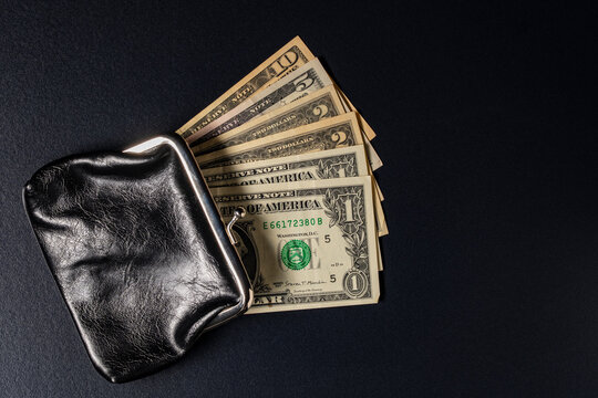 US dollar banknotes fanned out black vintage leather purse. American dollar bills including one five and ten notes fanning out of open retro black leather coin purse. Financial concept, copy space