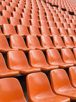 Empty orange plastic seats in a large outdoor stadium or arena stand.