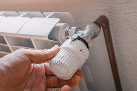 Hand adjusting a thermostatic radiator valve to control home heating temperature efficiently. Energy saving concept.