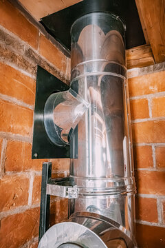 Stainless steel chimney flue pipe installed against a red brick wall inside a residential home, passing through the ceiling. Home renovation concept.