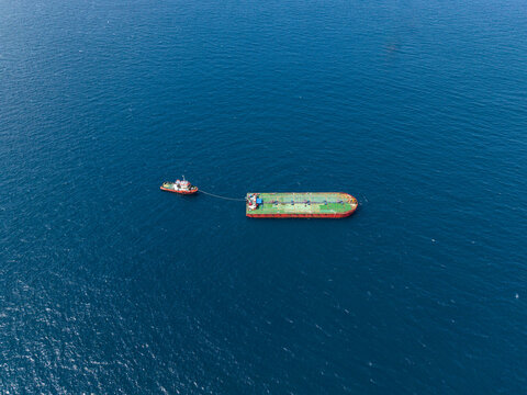 Aerial view of a tugboat towing a large cargo barge through the deep blue waters near Manggis Port, Manggis, Bali, Indonesia.