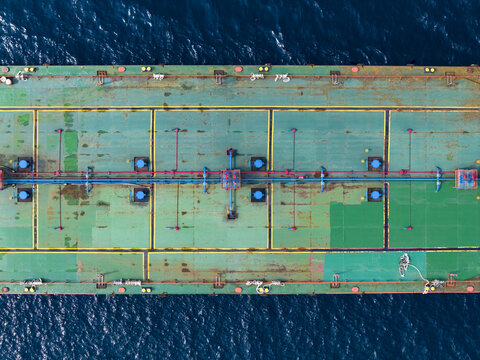 Aerial view of the deck of a cargo ship at Manggis Port, featuring green metal surfaces, blue piping, and industrial equipment, surrounded by the deep blue sea in Manggis, Bali, Indonesia.