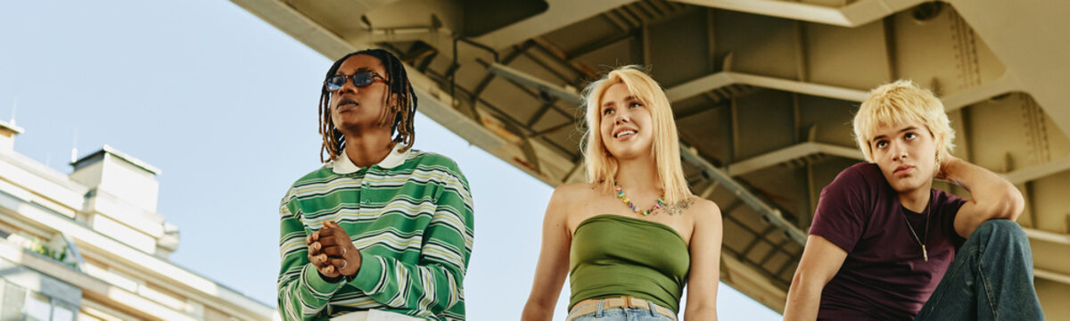 Diverse Gen Z people standing outdoors under bridge, looking away. Image represents youth culture and urban lifestyle, suitable for youth-targeted marketing campaigns, low angle view