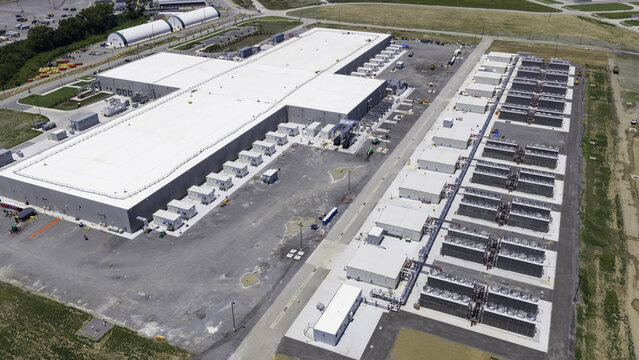 Aerial view of a modern data center campus with a large facility building, an electrical substation, and rows of cooling infrastructure units in Gallatin, Tennessee, United States.