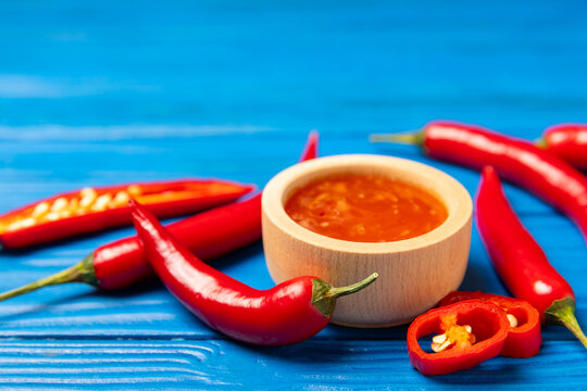 Hot chili sauce  in a bowl with fresh red peppers and chili flakes on wooden cutting board. Chili sauce. Cooking concept. Natural red homemade sauce. Sauce splash isolated on a white background. 