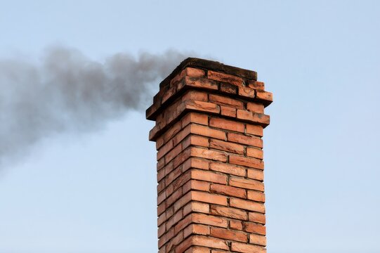 Brick chimney emitting dark smoke polluting clear sky