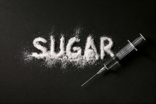 'Sugar' word sprinkled with sugar crystals with an insulin syringe on black background. Diabetes and sweet addiction concept. Top view for poster, design