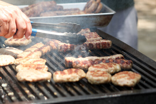 Traditional Bulgarian grilled minced meat kebapche and meatballs cooking on a smoking outdoor barbecue grill close up.