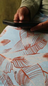 Close up of a person holding a smartphone while sitting on a patterned fabric.