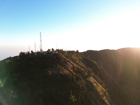 Aerial view of Mount Bromo area featuring communication towers on a mountain ridge with lush vegetation and golden hour sunlight in Tosari, East Java, Indonesia.