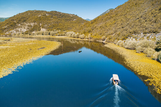 Aerial view of a boat traveling on Rijeka Crnojevica river, Skadar lake national park, Montenegro, surrounded by mountains and wetlands