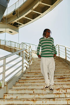 Young adult African American man walking down outdoor stairs in city, listening to music. Low angle view representing active lifestyle, youth culture, and urban mobility, vertical