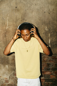 Young African American man wearing headphones outdoors, looking down and listening to music. Image suitable for youth culture and audio technology marketing campaigns, vertical