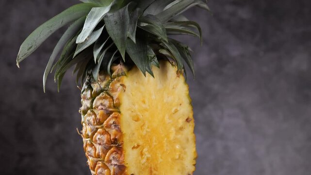 Rotating shot of a whole fresh pineapple with green leaves on a dark studio background.