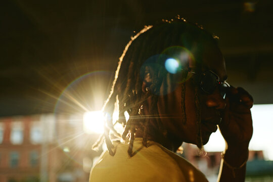 Young adult African American man with dreadlocks wearing sunglasses outdoors at sunset, representing youth culture. Image ideal for Gen Z lifestyle marketing, close up shot