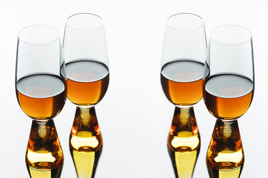 Four glass glasses with an amber alcoholic drink on white background with perfect reflection. Amber liquid. Studio photography of alcoholic beverages in close-up