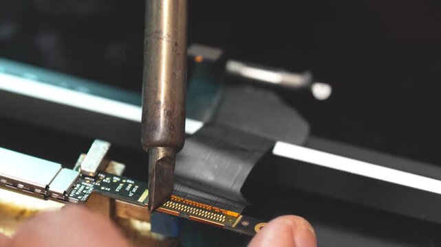 Close-up technician cleaning laptop connector with tools in electronics repair workshop