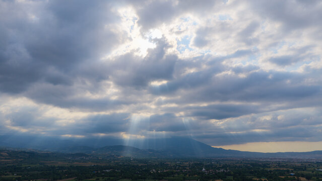 Dramatic rays of sunlight filtering through the clouds into the valley (the Tyndall effect). A magnificent photograph of the sky and landscape.