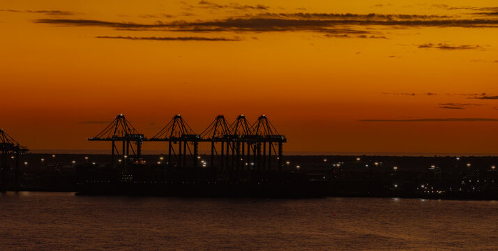 Aerial view of DP World Caucedo container port with silhouetted cranes against an orange sunset sky over the Caribbean Sea in Boca Chica, Santo Domingo Provinc, Dominican Republic.