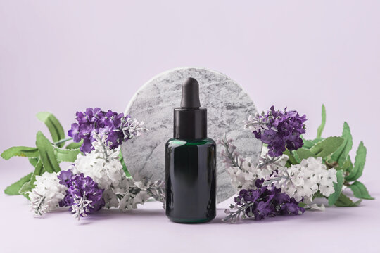 Dark green glass essential oil or serum dropper bottle dropper bottle mockup with purple flowers and round marble podium on a soft pastel background, skincare, wellness, and aromatherapy
