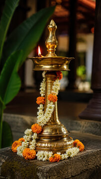 Traditional brass nilavilakku oil lamp with jasmine marigold garland, onam harvest festival decor in kerala courtyard, pookalam floral carpet, sadya feast celebration, prayer flame, culture