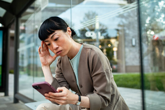 Worried woman reading smartphone at bus stop