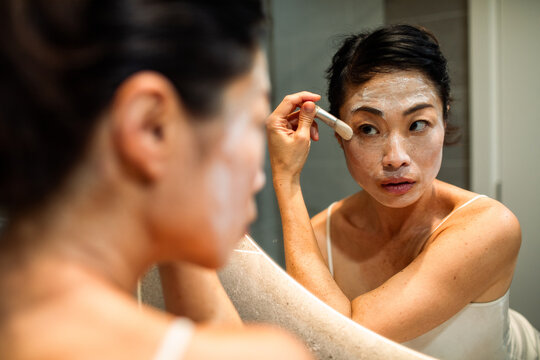Woman applying facial mask with brush in bathroom mirror