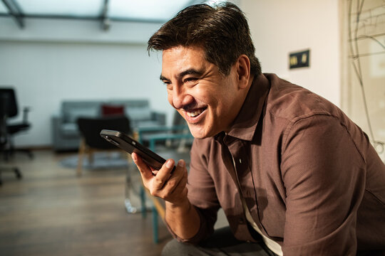 Smiling middle-aged man using voice assistant on smartphone at home