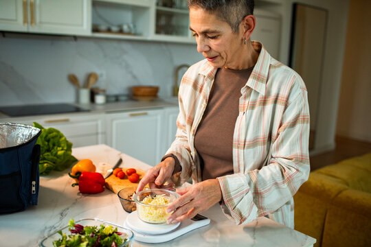 Mature woman weighing shredded cheese at home kitchen counter