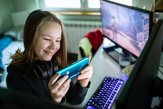 Smiling teenage girl gaming on smartphone at home desk