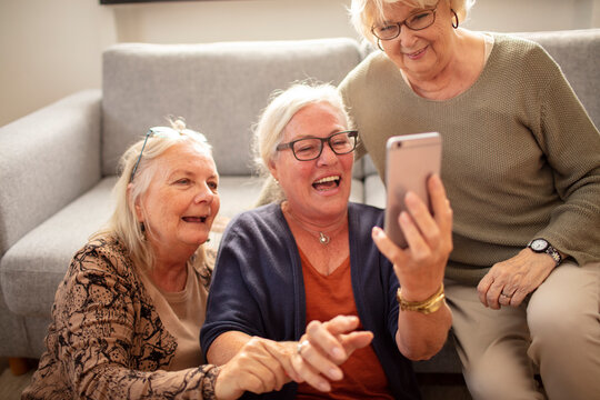 Three senior women laughing over a smartphone at home